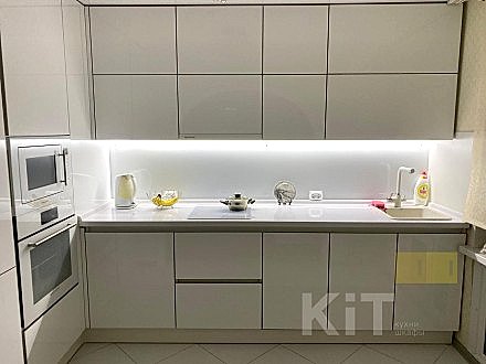 Современная угловая кухня с белыми глянцевыми фасадами и белым фартуком из закаленного стекла - фото - 1